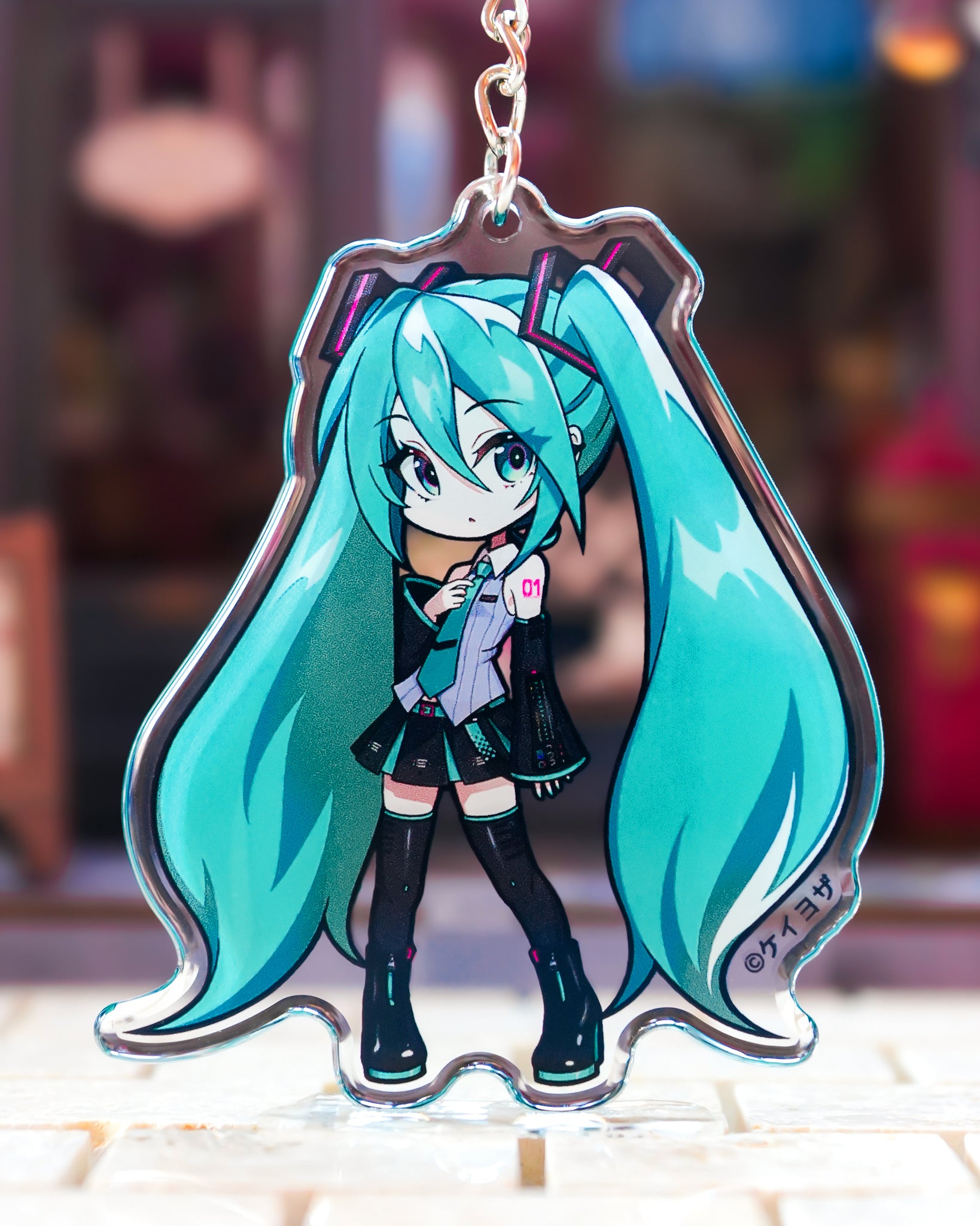 Anime character keychain with long turquoise hair and a blurred background Hatsune miku v6 acrylic charm chibi art