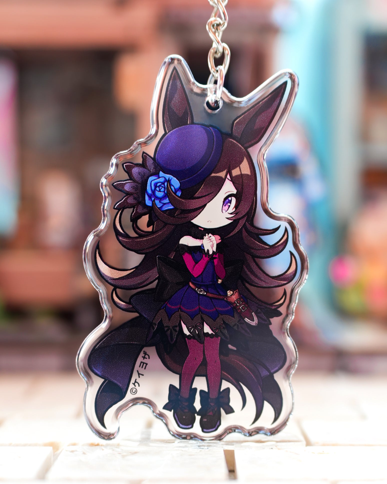 Anime character keychain with long hair and purple outfit on a blurred background racing horse chibi Uma musume pretty derby